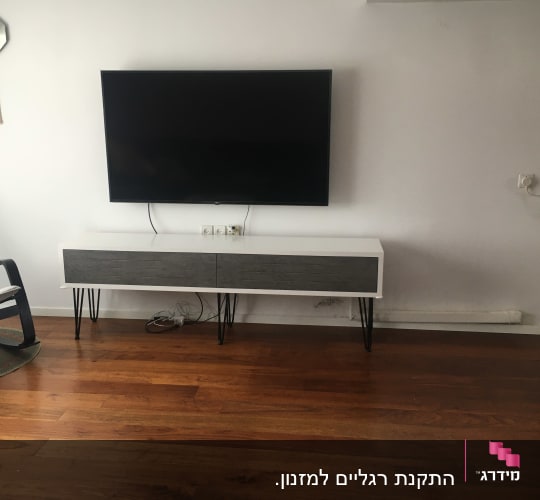 טלוויזיה תלויה על קיר מעל שידה מעץ
